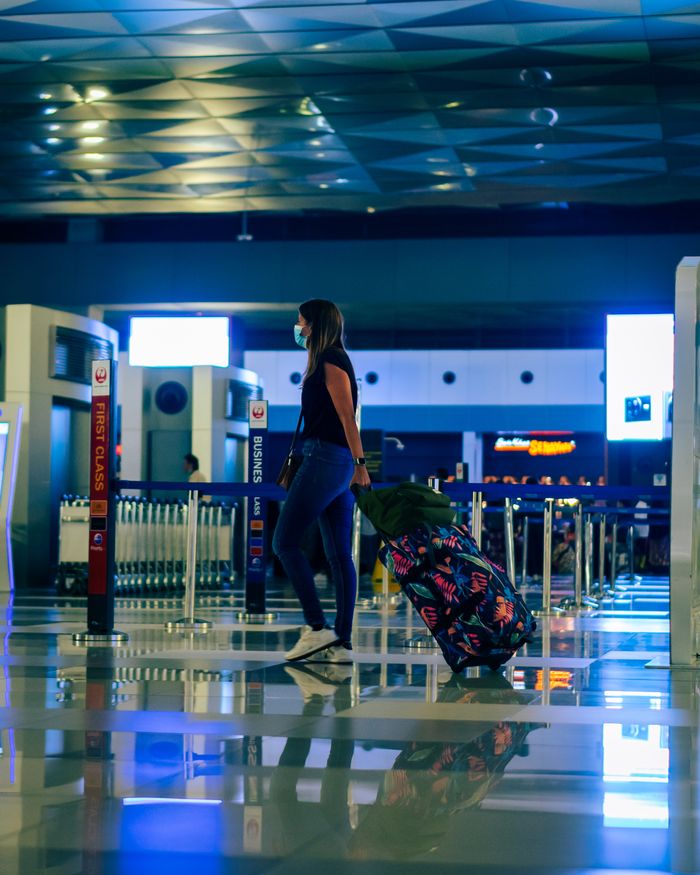 Services A woman wearing a face mask walks through an airport with luggage, reflecting modern travel trends.