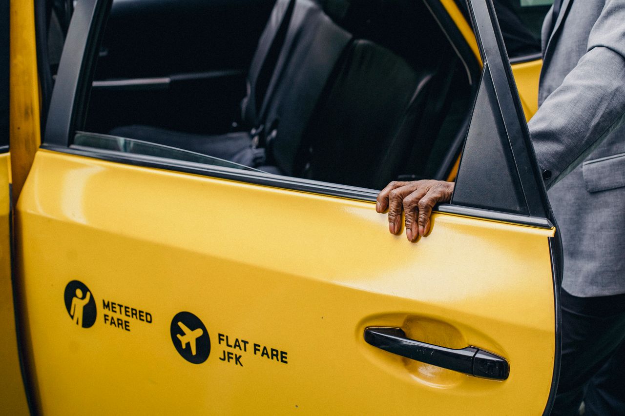 Services A person opens a yellow taxi door with JFK flat fare signage.